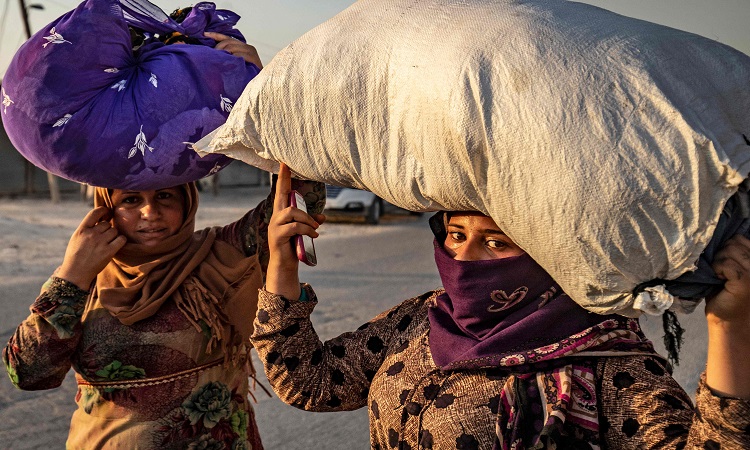 Civilians carry their belongings over their head as they flee Ras al-Ain on October 9, 2019. Photo: AFP / Delil Souleiman
